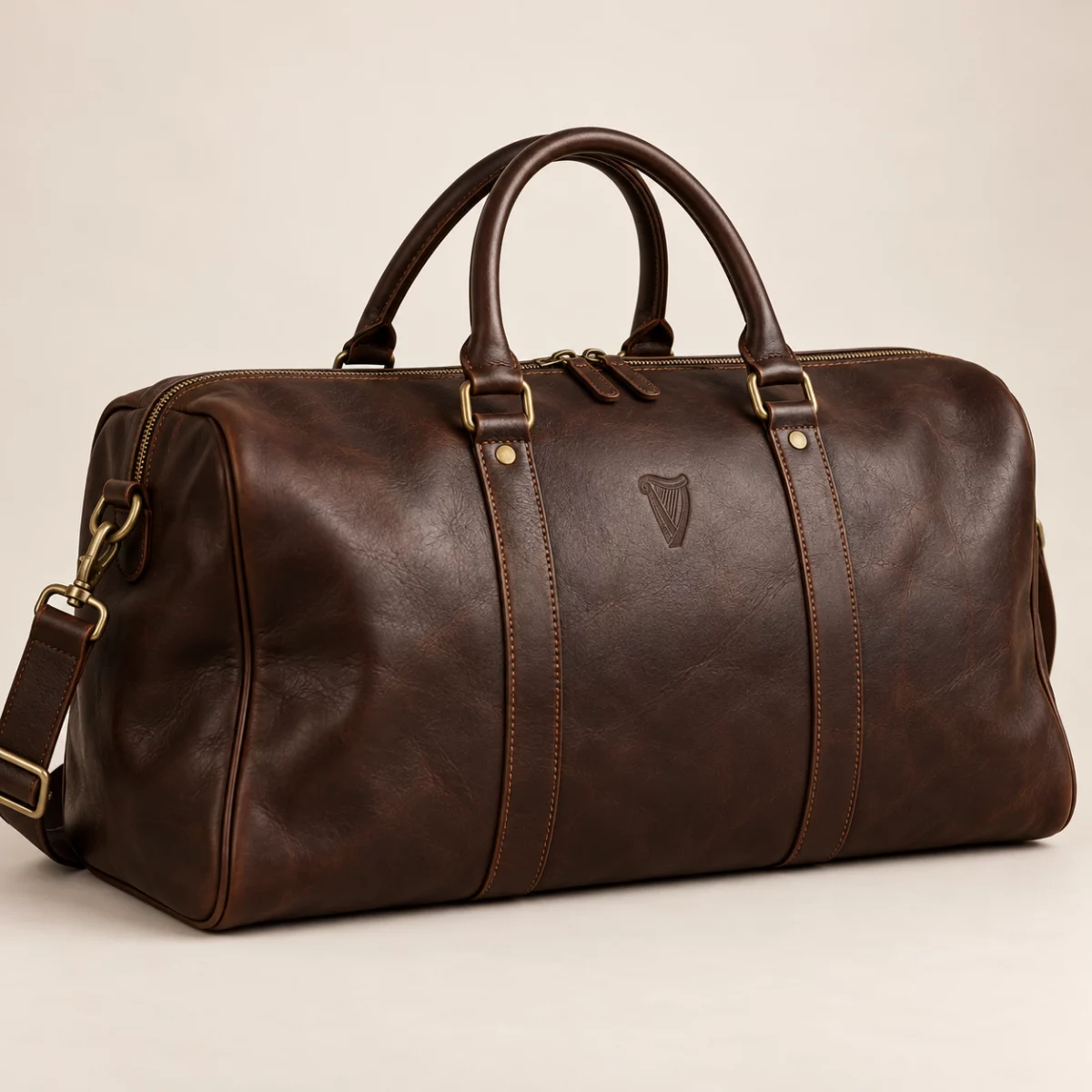Heritage Signature Weekender Dark brown Heritage Signature Weekender design mock-up: Dark-brown leather-look weekender; small embossed-look harp; muted brass hardware
